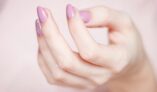 A close-up of a woman's hand showing a stylish pink and glittery manicure.